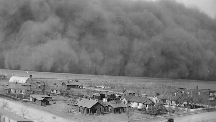 Black-and-white photograph of a towering Dust Bowl dust storm approaching a rural town.